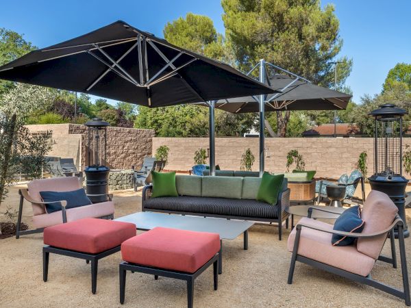 Outdoor patio with cushioned lounge seating, large black umbrellas, a table, and an outdoor grill in a sunny backyard.