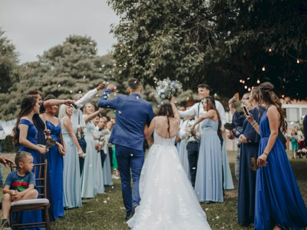 An outdoor wedding celebration: the bride and groom in blue and white as guests cheer and toss confetti.