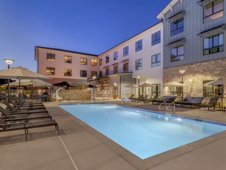 Evening pool deck at a modern hotel, with loungers, umbrellas, and a blue-lit swimming pool against a sleek building.