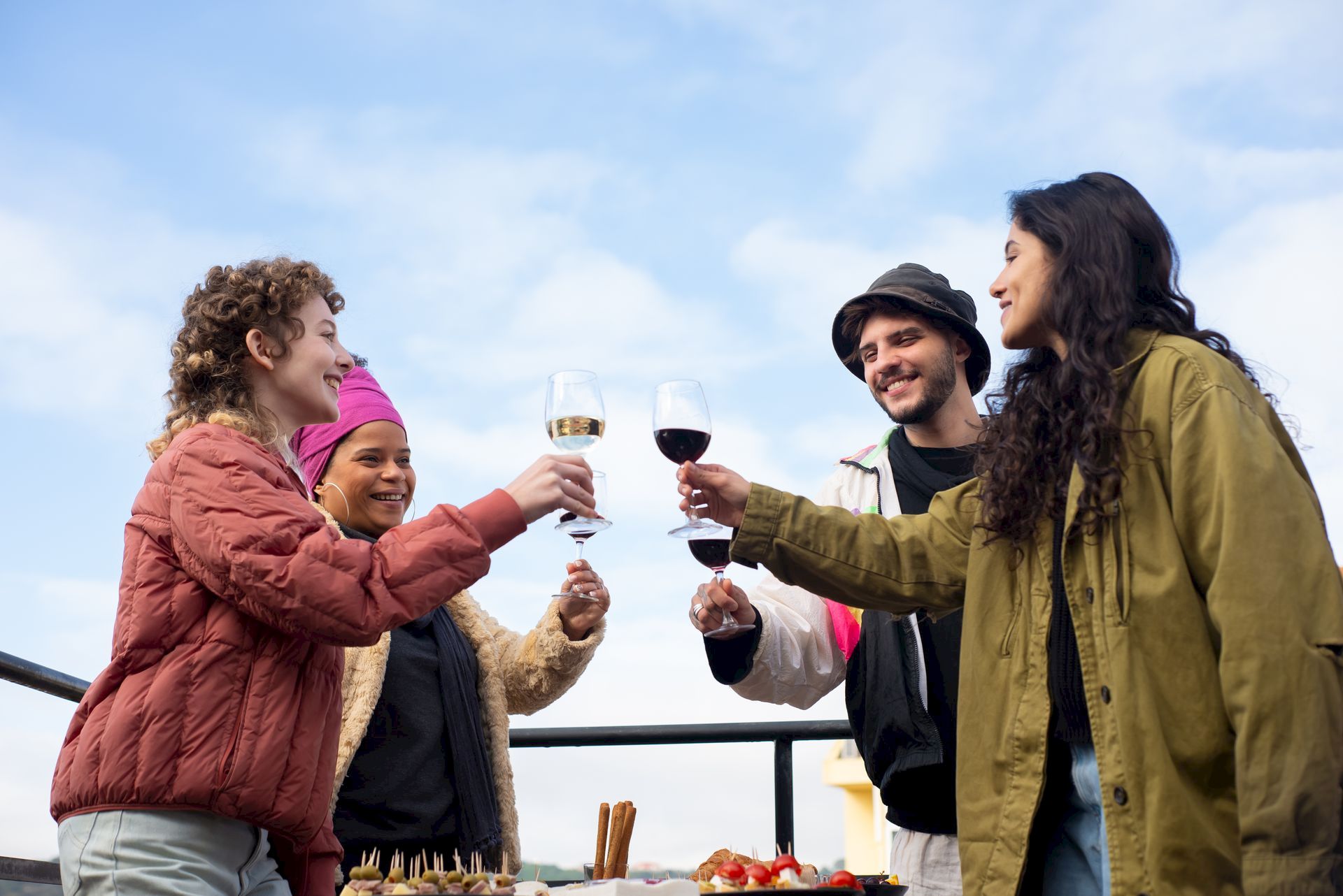 A group of friends outdoors cheer with glasses of wine during a celebration against a blue sky.